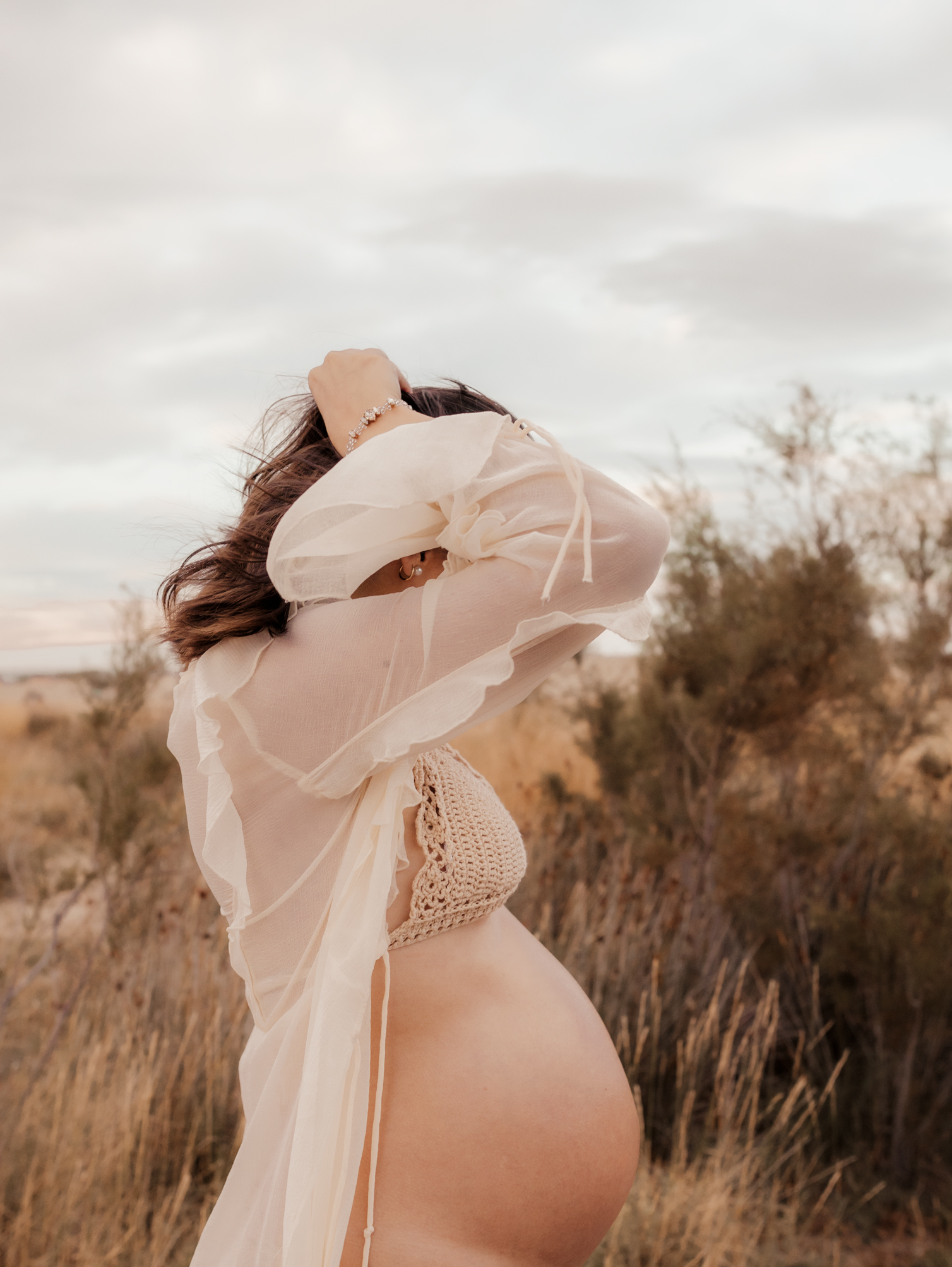 Séance photos de grossesse pour future maman dans un paysage naturel avec des herbes et un ciel à la douce lumière naturelle