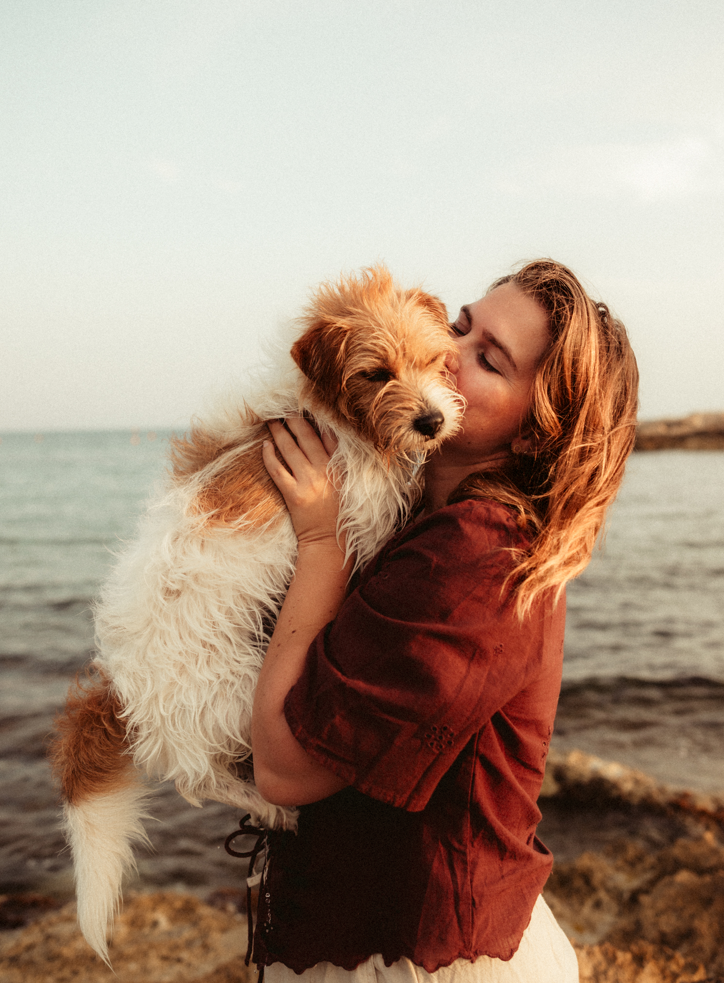Séance photo pour chien et maître à Carry le Rouet. Une femme embrasse un chien tout en le tenant dans ses bras, sur une plage avec la mer en arrière-plan.